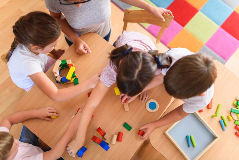 Preschool teacher with children playing with colorful wooden blocks