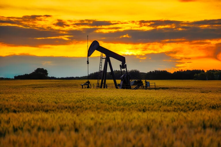 An oil pump jack on the middle of the wheat field with the beautiful sunset sky